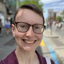 Linnea profile photo (white woman with glasses and short hair standing on a sunny street)
